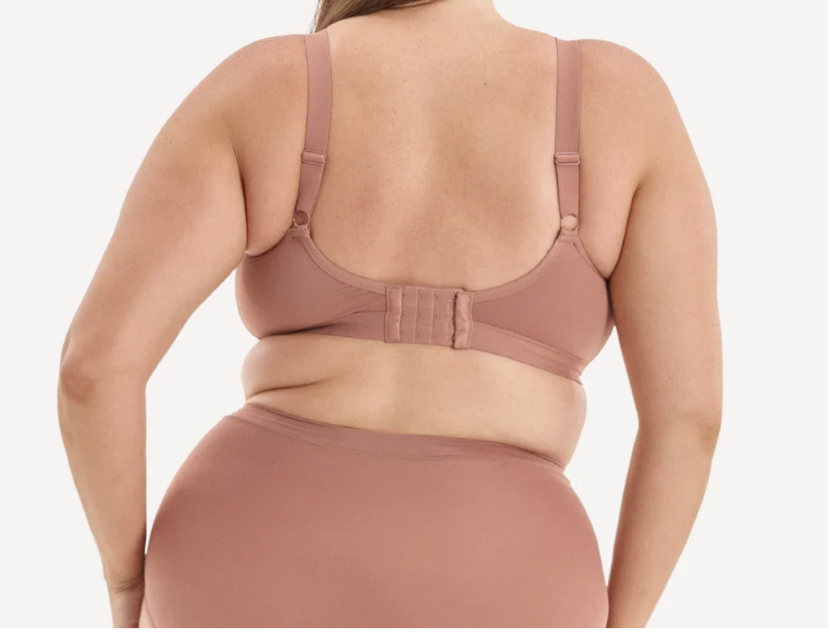 A woman shown from the back wearing a dusty rose/nude bra and matching underwear against a clean light gray studio background.