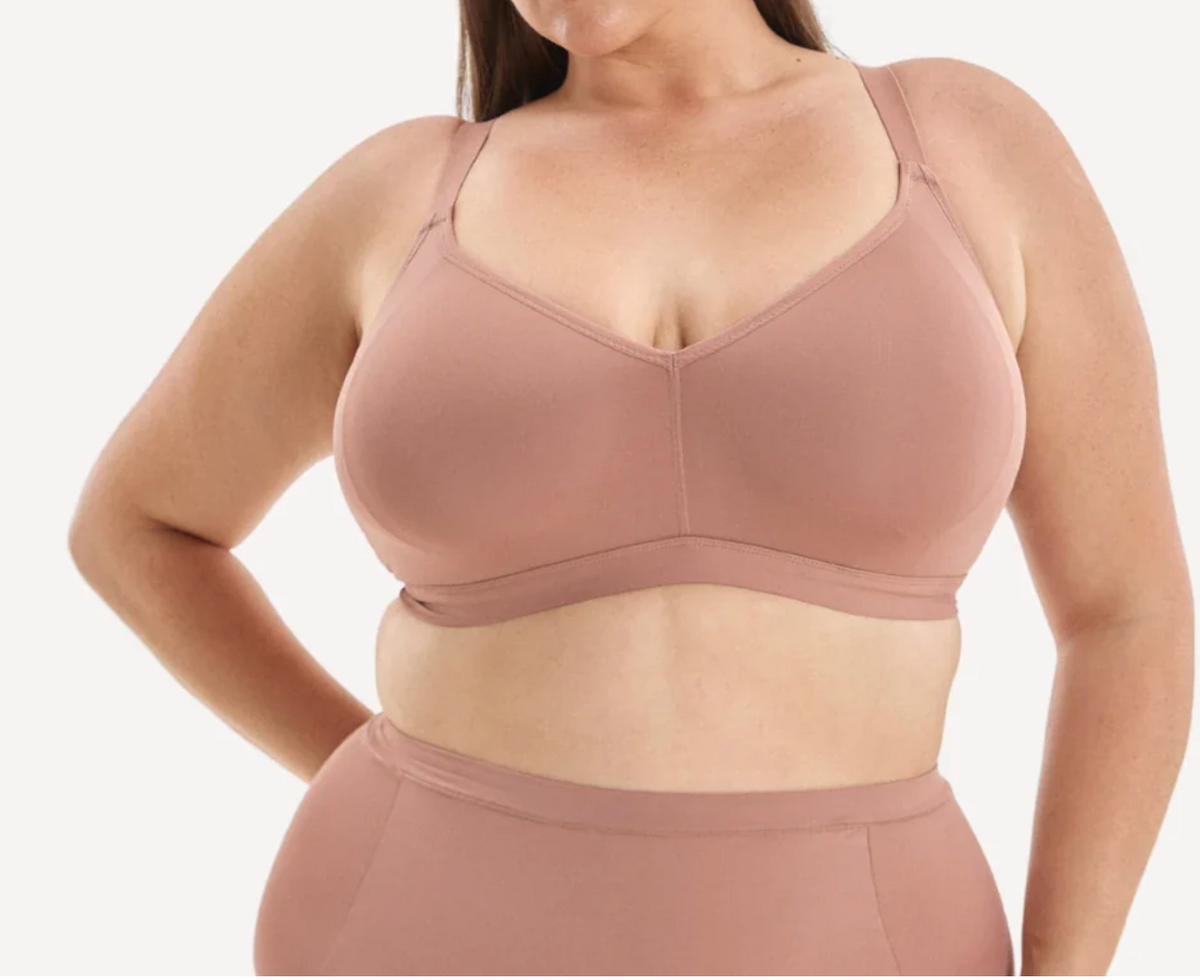 A plus-size model wearing a dusty rose pink wireless bra and matching high-waisted briefs against a clean white background.