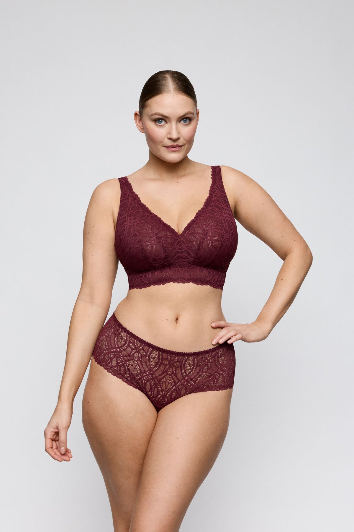 Woman wearing a burgundy lace lingerie set on a plain background