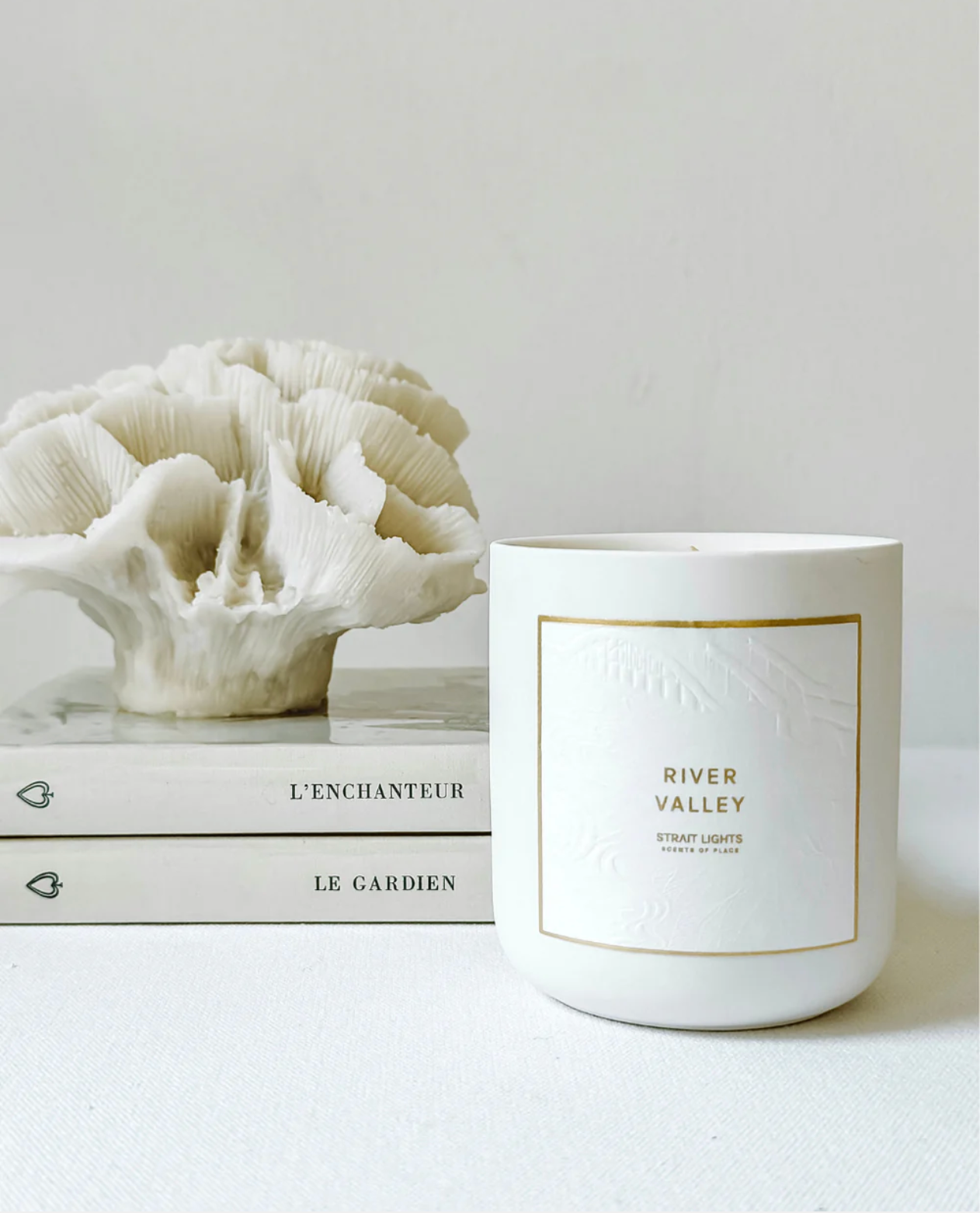 White candle labeled 'River Valley' next to a decorative coral piece on a light gray background