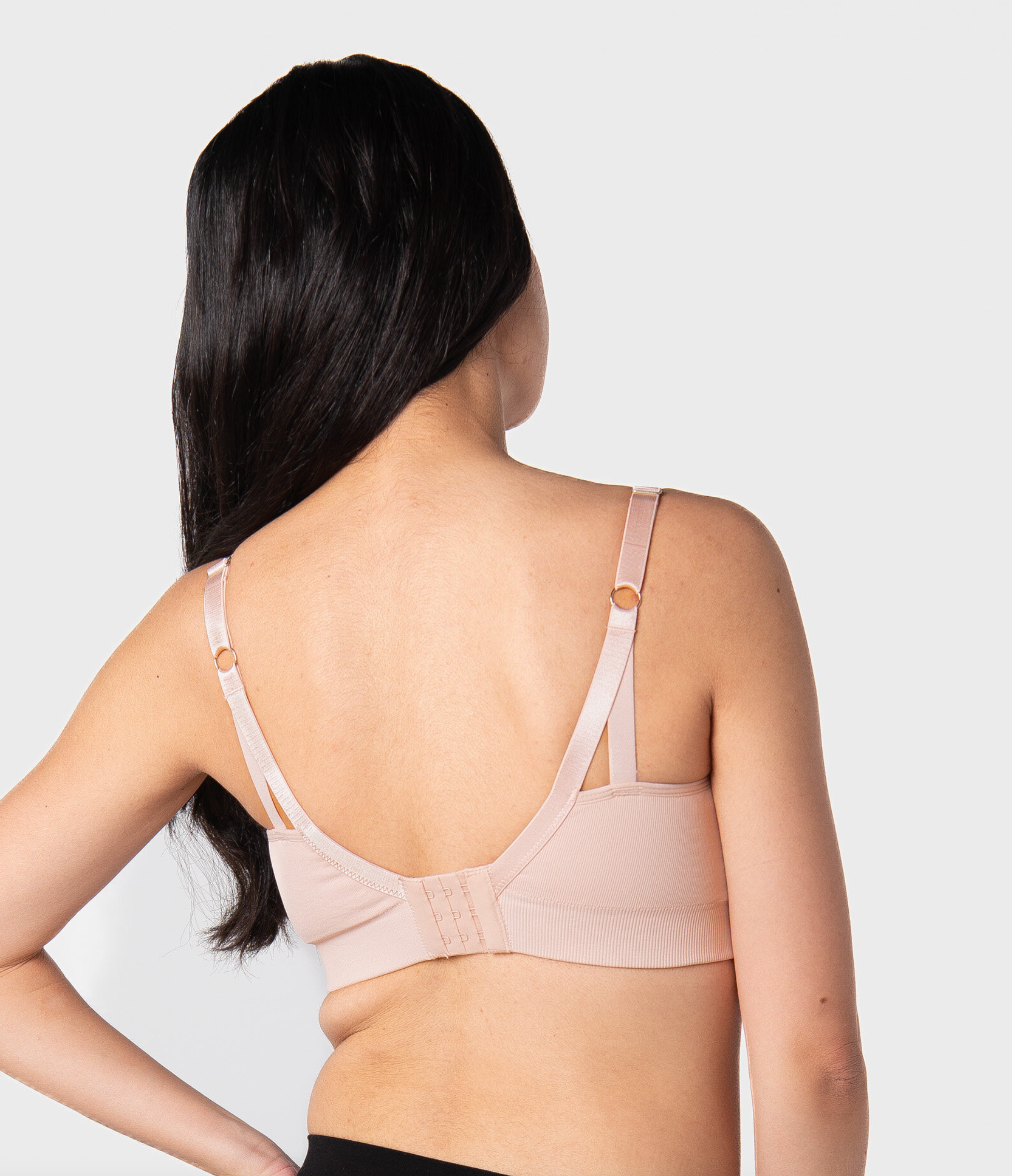 Woman wearing a ballet pink nursing bra against a light gray background