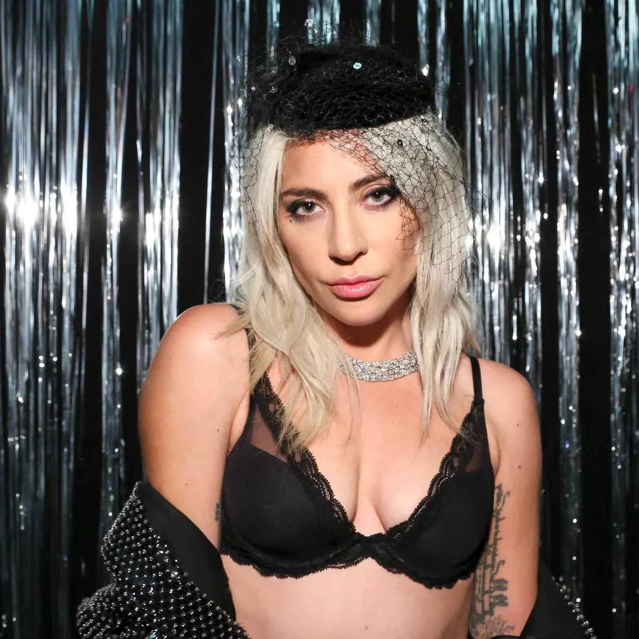 Person wearing a black bralette against a silver tinsel background