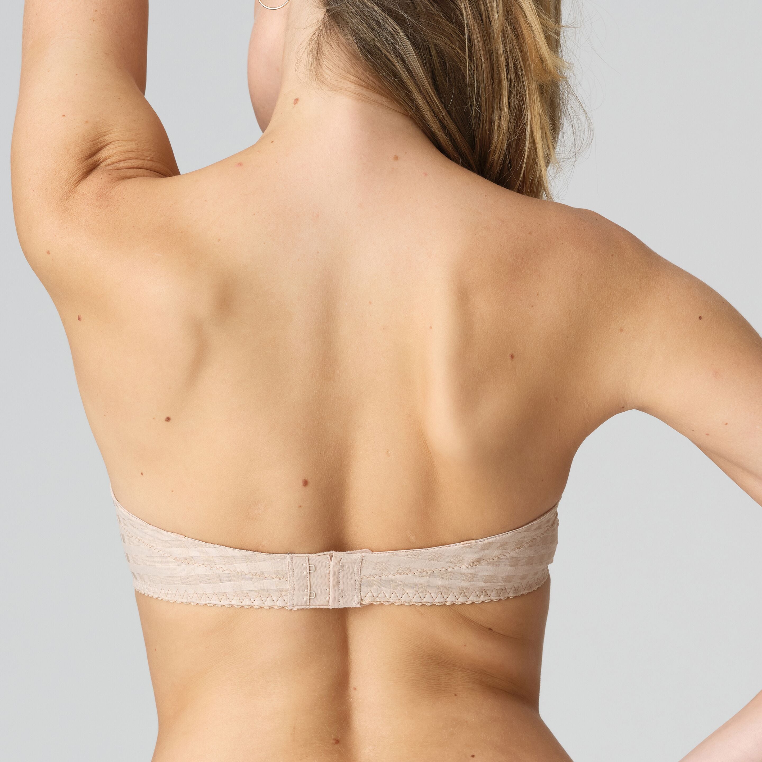 Beige strapless bra worn by a person on a light gray background