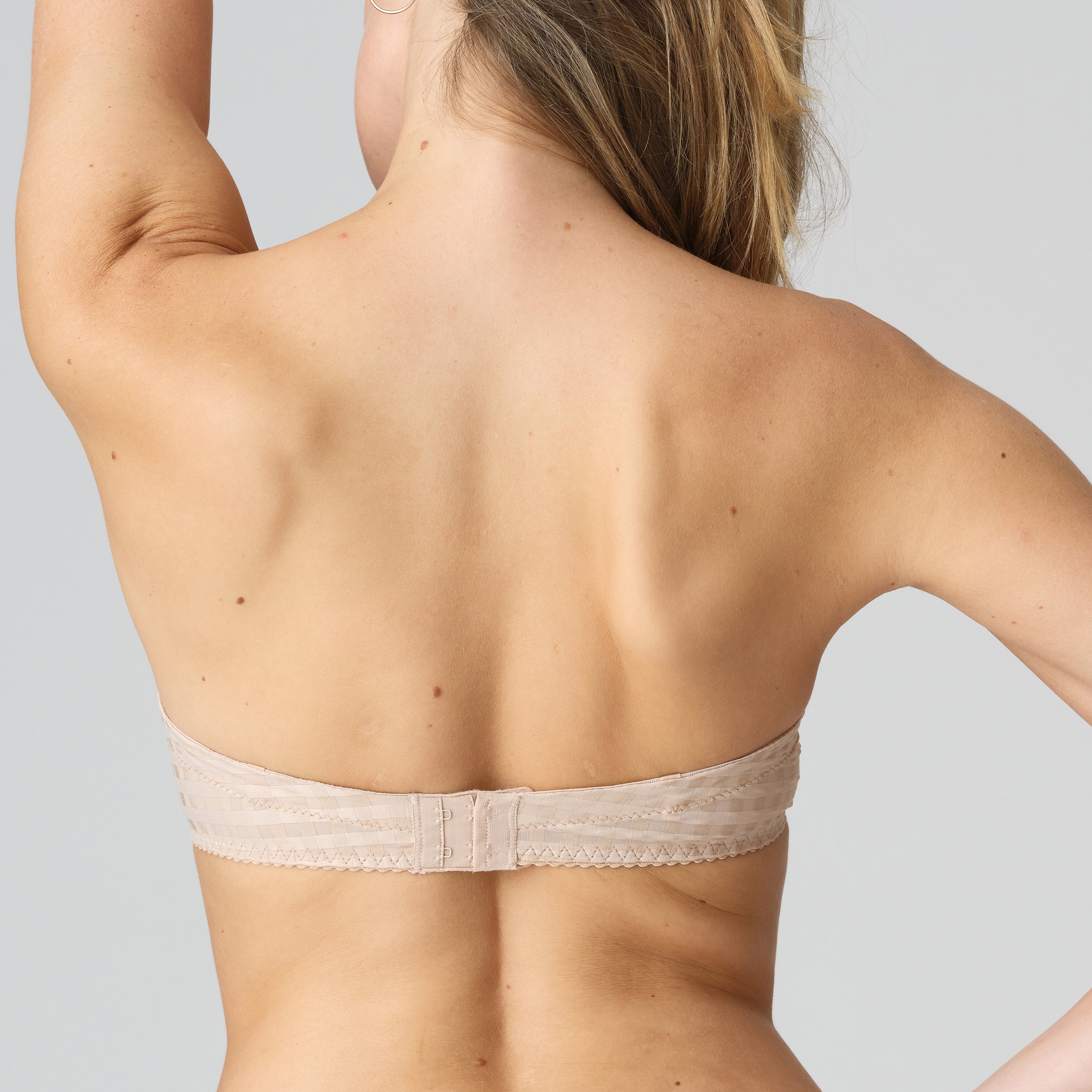 Woman wearing a beige strapless bra against a plain background