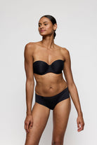 Woman wearing a black strapless bra and high-waisted underwear on a white background