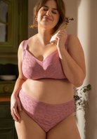 Woman wearing a pink lace lingerie set in a softly lit room.