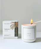 Lit candle with 'Tanglin' branding next to its packaging on a light gray background