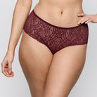 A close-up of a model wearing burgundy lace underwear against a light gray studio background.